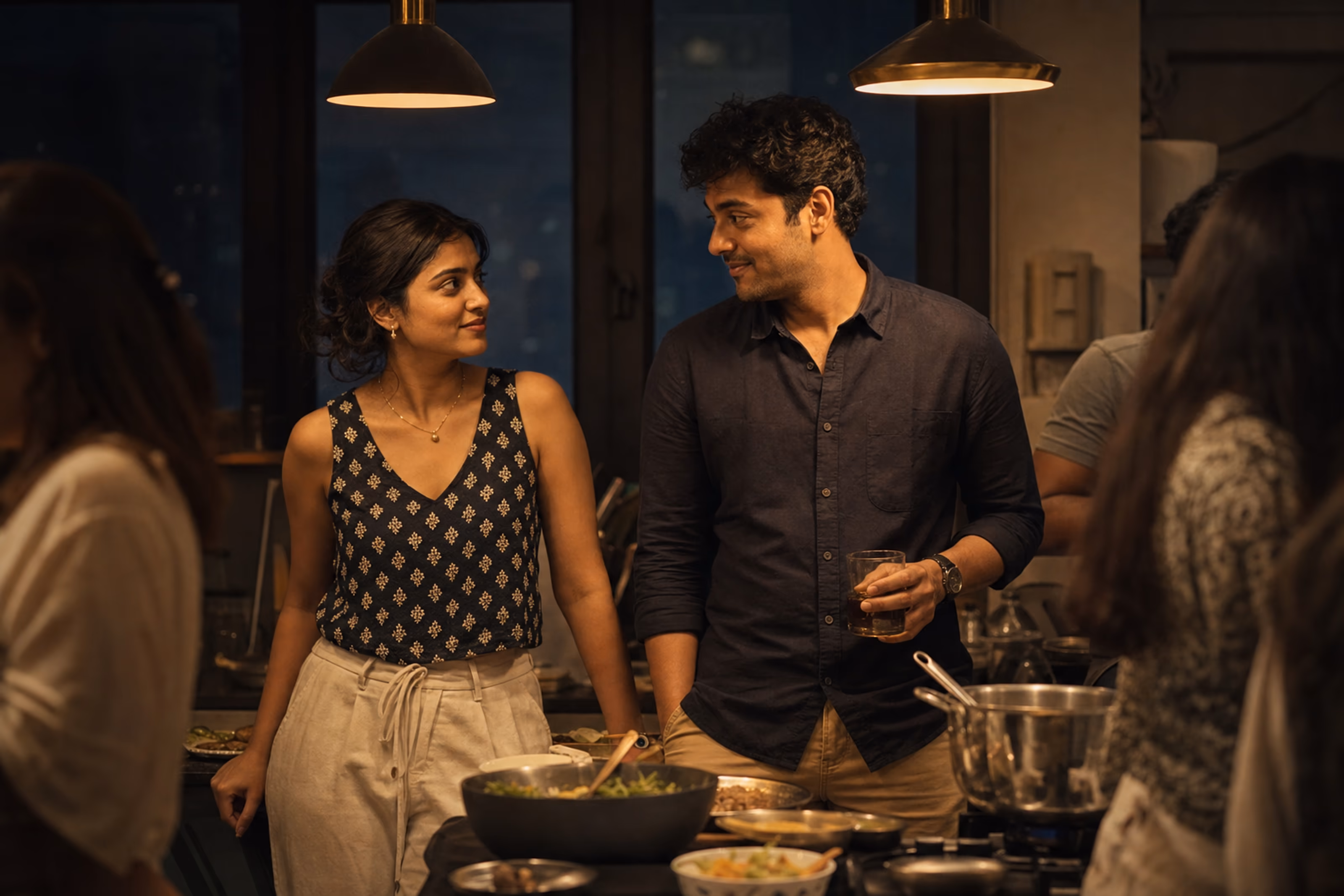 Aria and Dev noticing each other across an intimate kitchen party