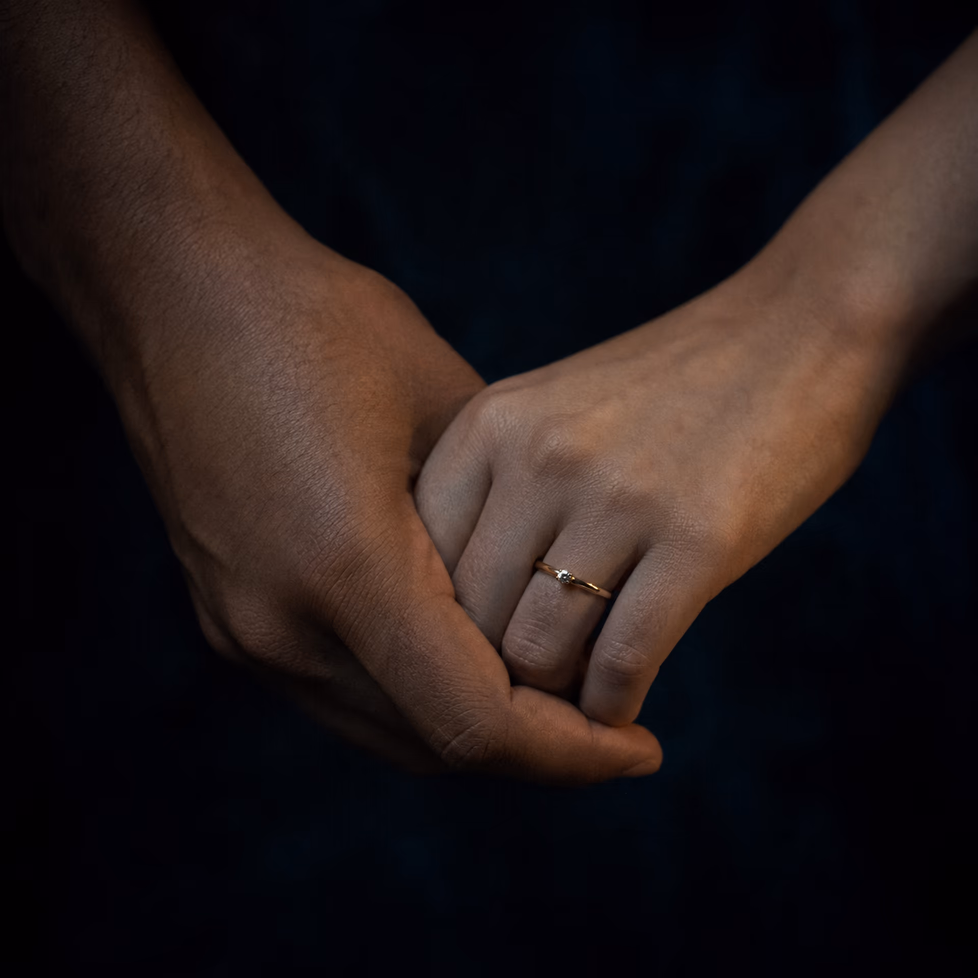 Two hands interlocked with one engagement ring in low warm light
