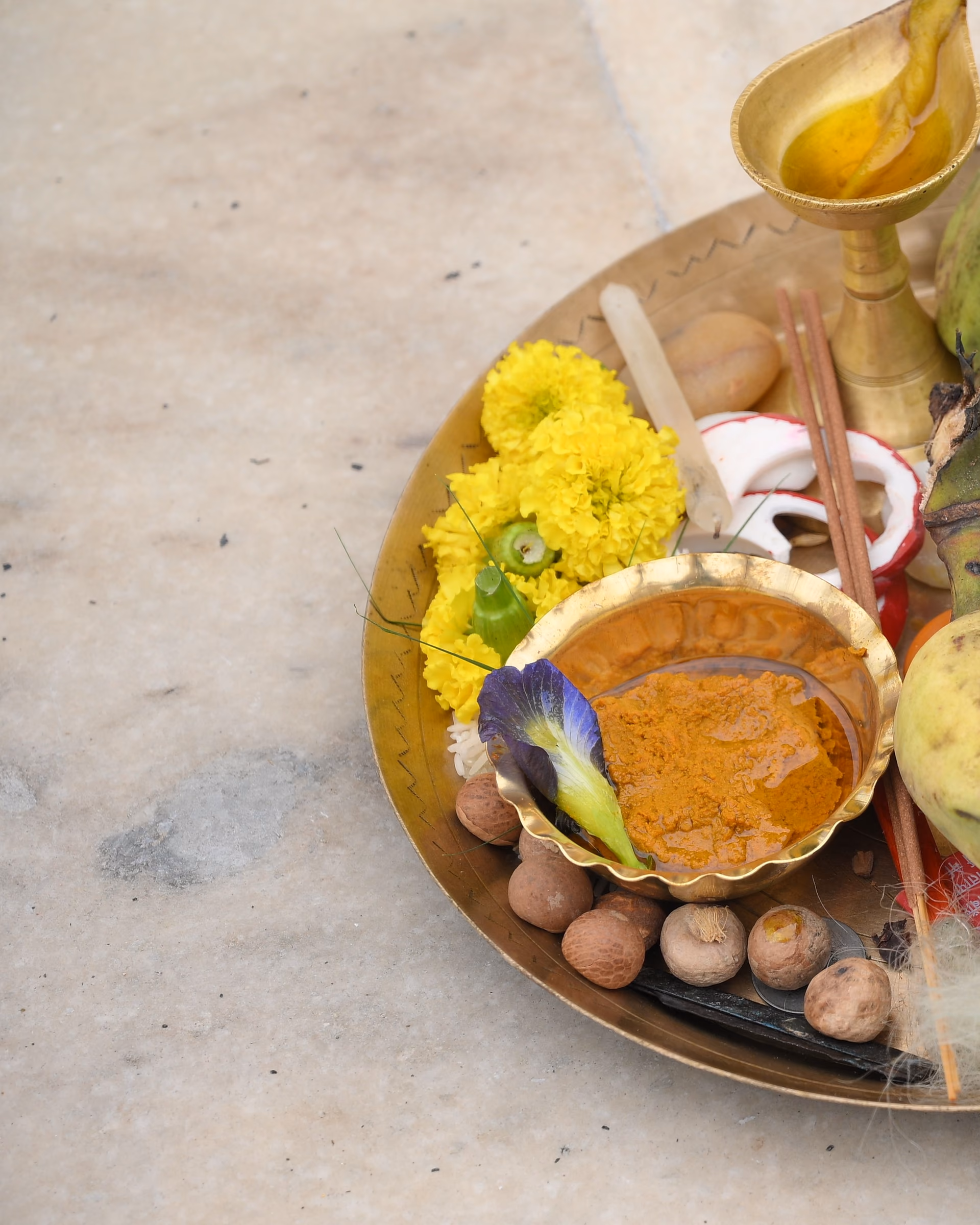 Turmeric paste in a brass bowl beside marigolds and a lit lamp.