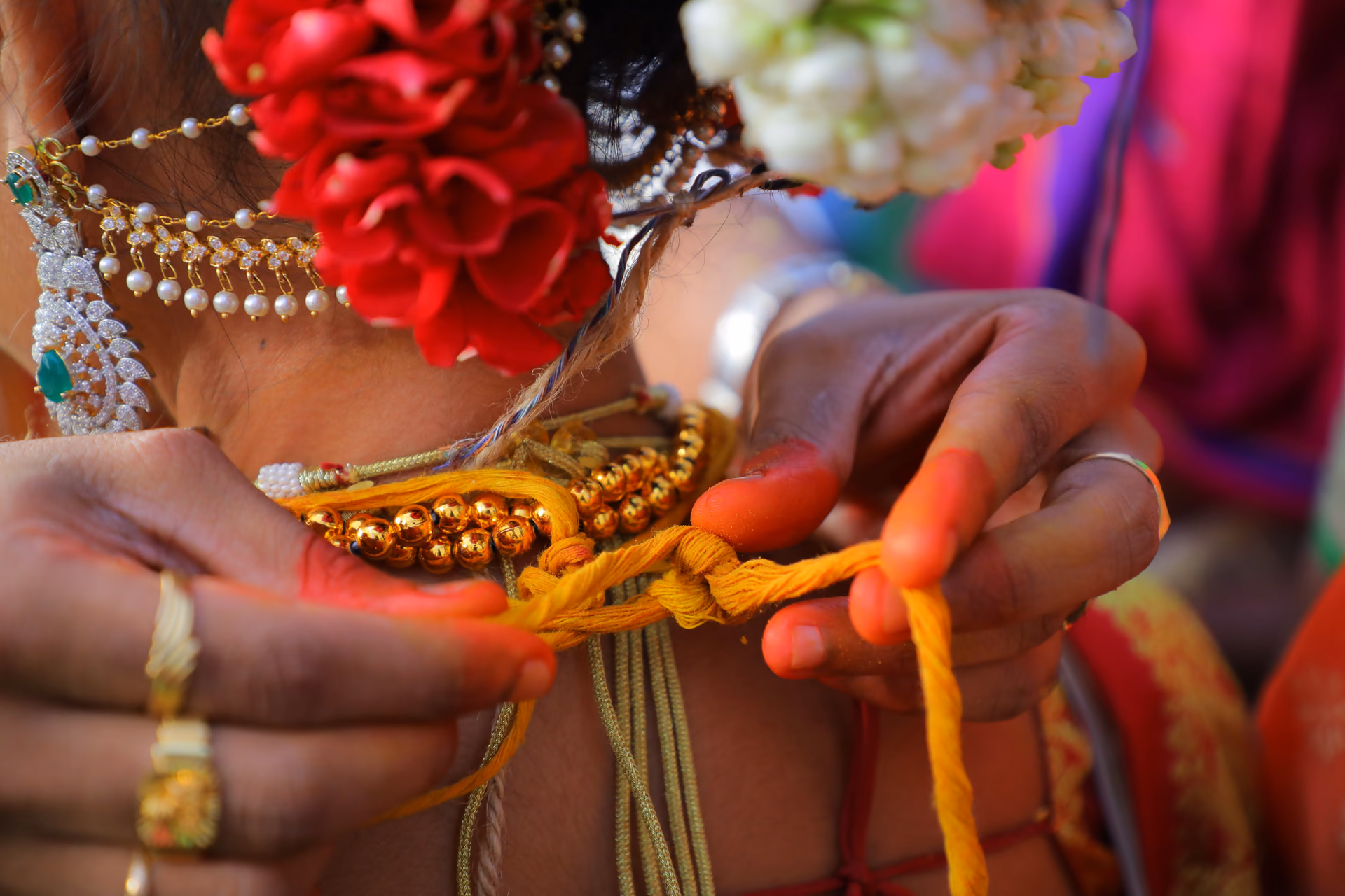 Hands tying the turmeric thread with its gold beads at the nape, jasmine in her hair.