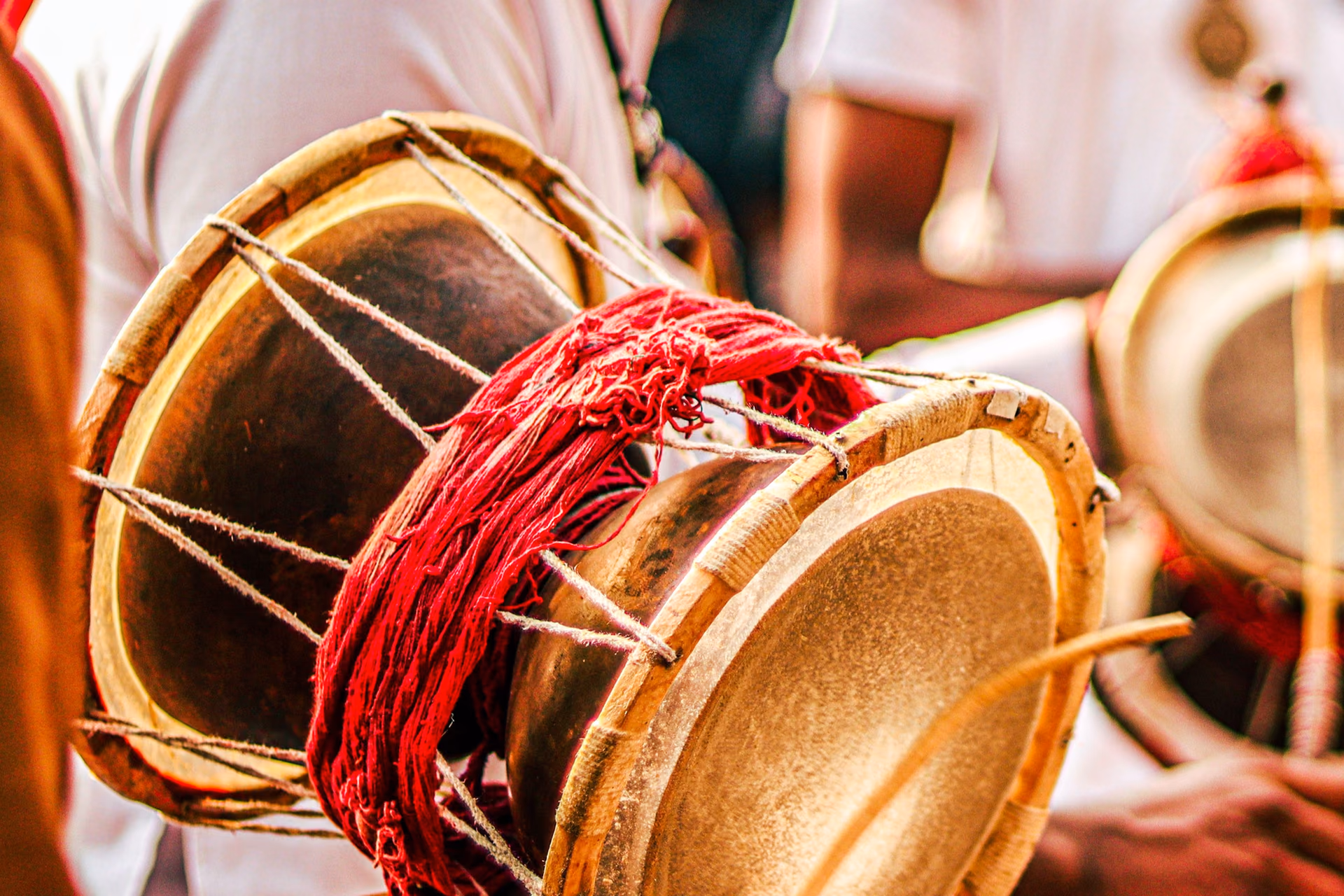 A dhol mid-stroke, red cord and stick, the drummers behind out of focus.