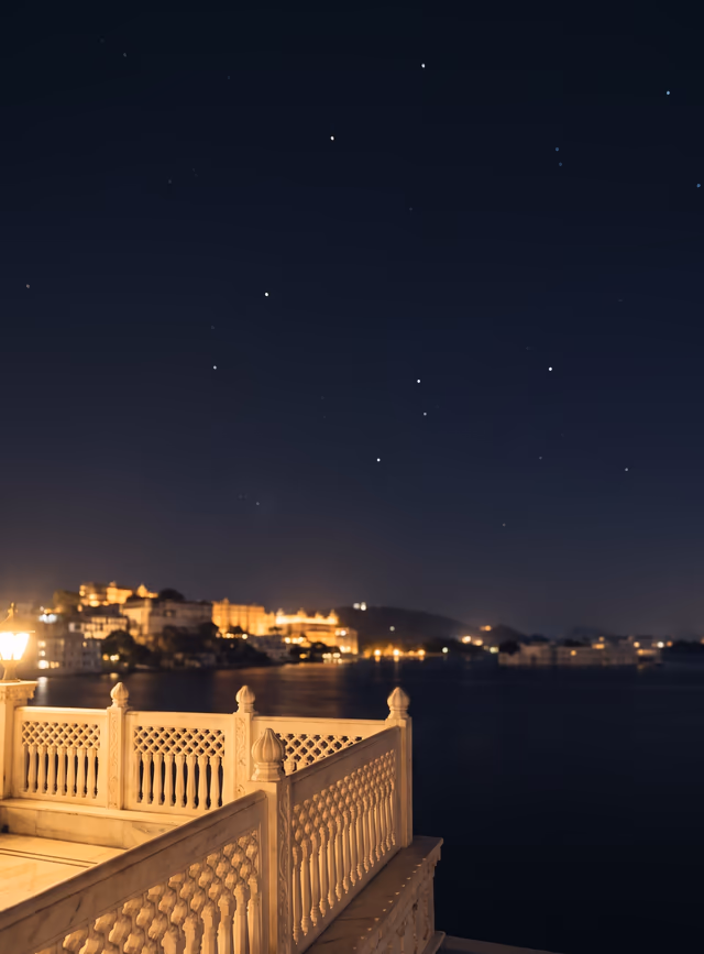 A white terrace edge overlooks Udaipur's dark lake, palace lights, and winter sky.
