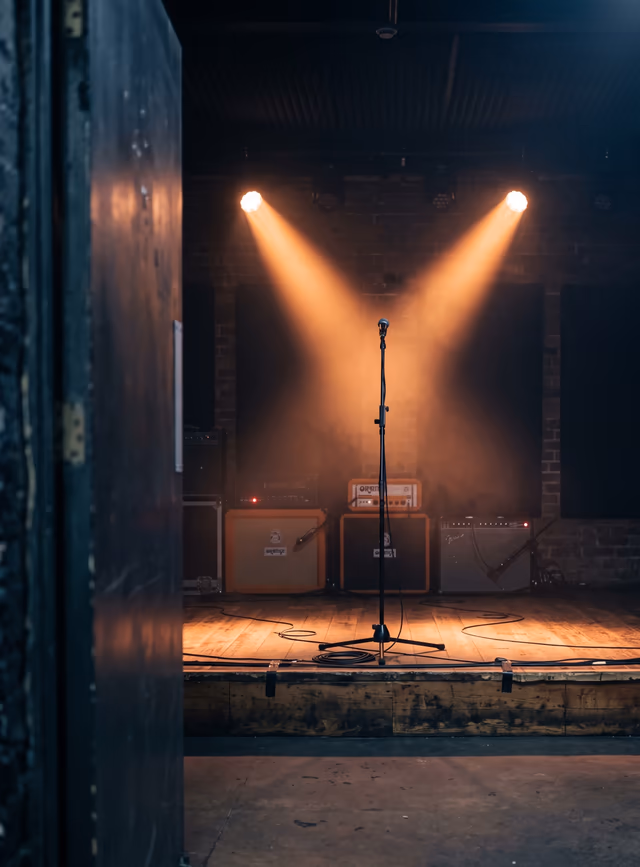 A propped stage door opens onto an empty hall crossed by amber beams.